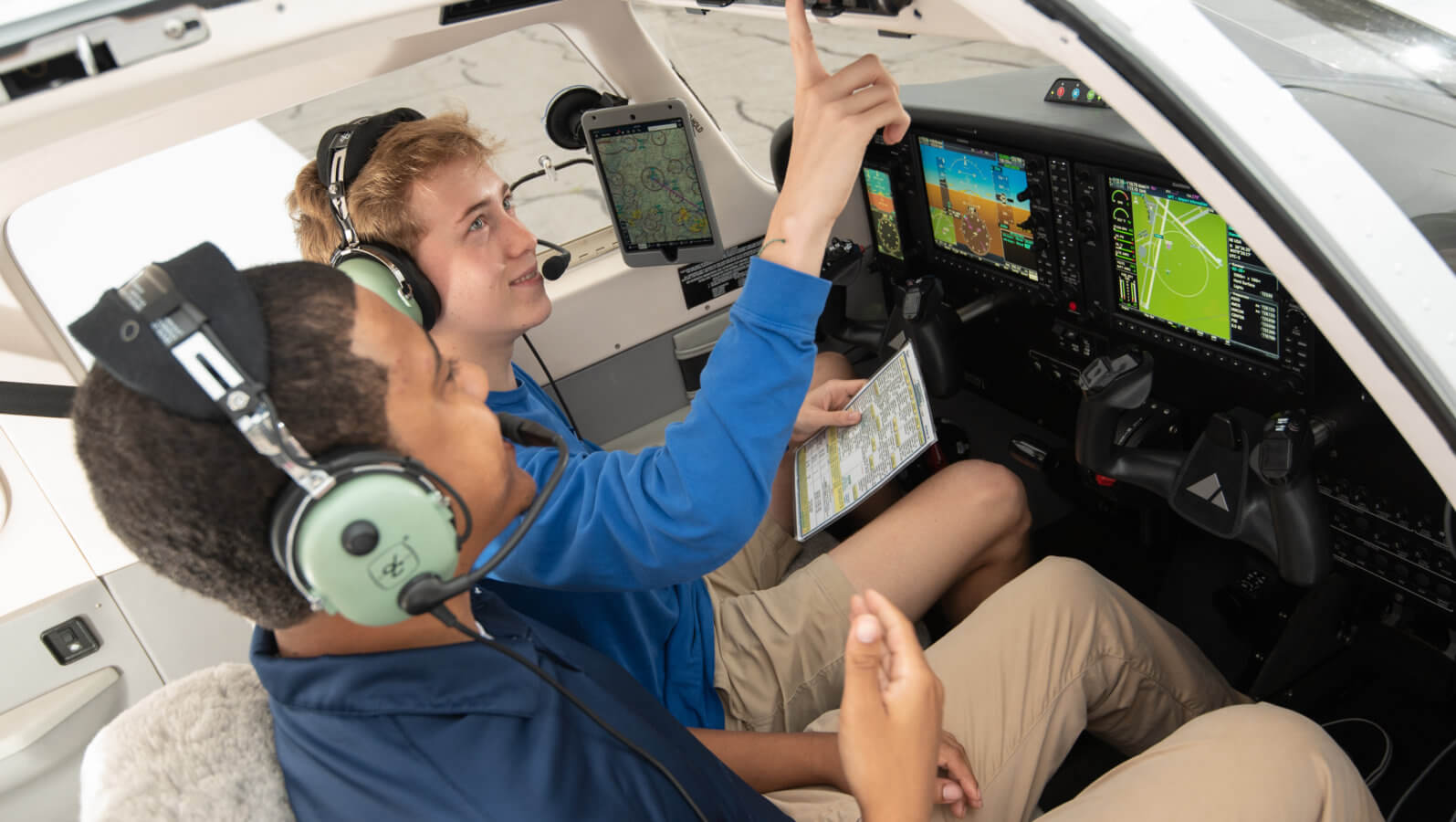 two AU students in a plane cockpit pointing to buttons
