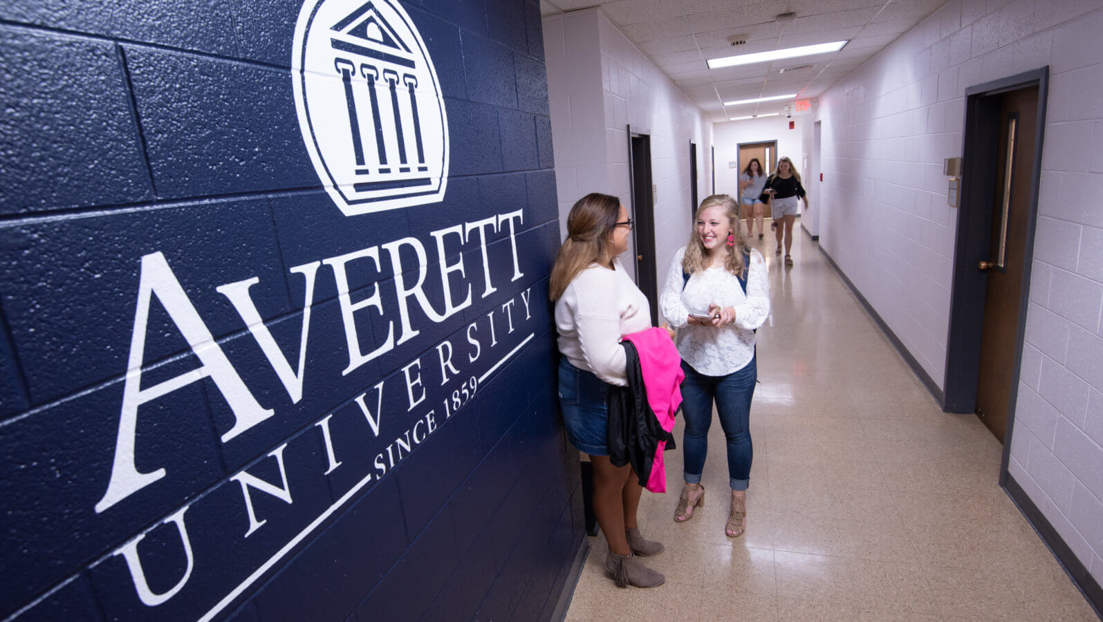 students talking in a hallway by the AU Logo on the wall