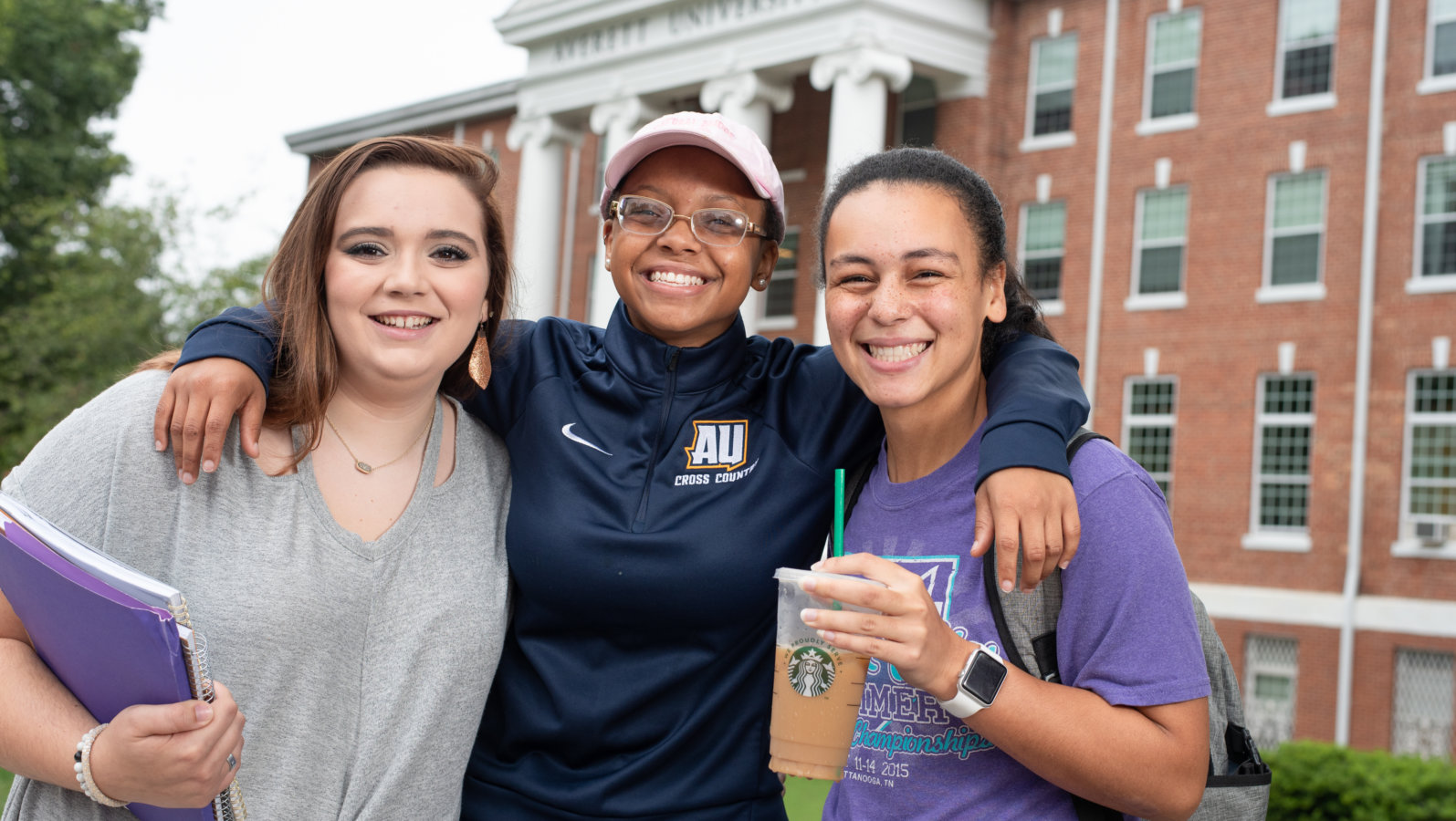 Three students smiling in front of AU main hall