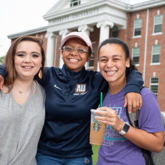 Three students smiling in front of AU main hall